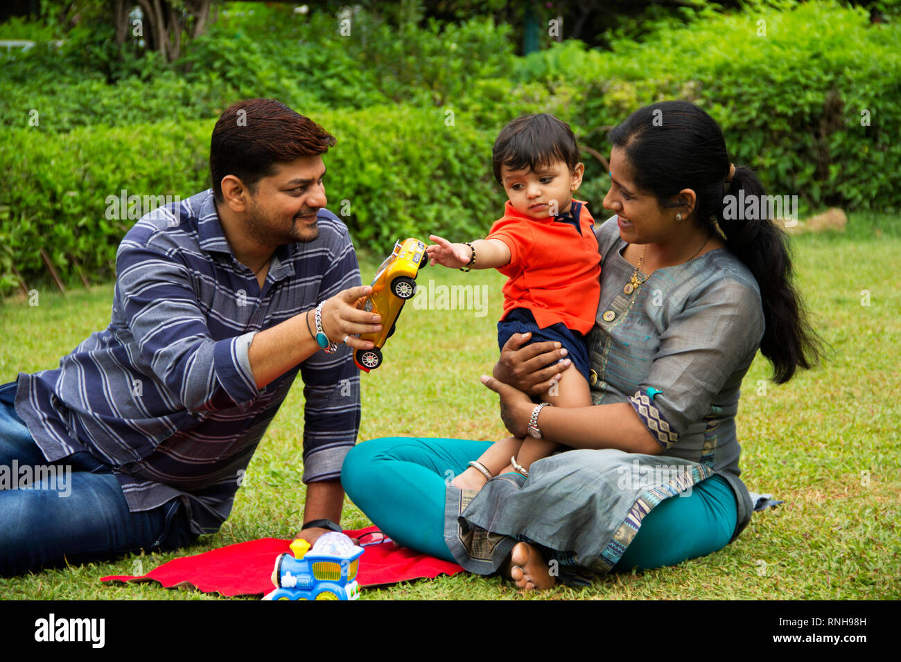 Heureux famille indienne, le père donnant à sa voiture jouet petit garçon, assis avec sa mère, à l'intérieur de jardin, Pune, Maharashtra Banque D'Images