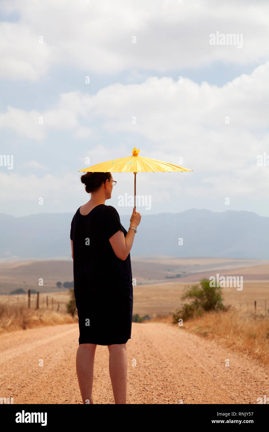 Mature Woman in Black Dress with Umbrella in Countryside Banque D'Images