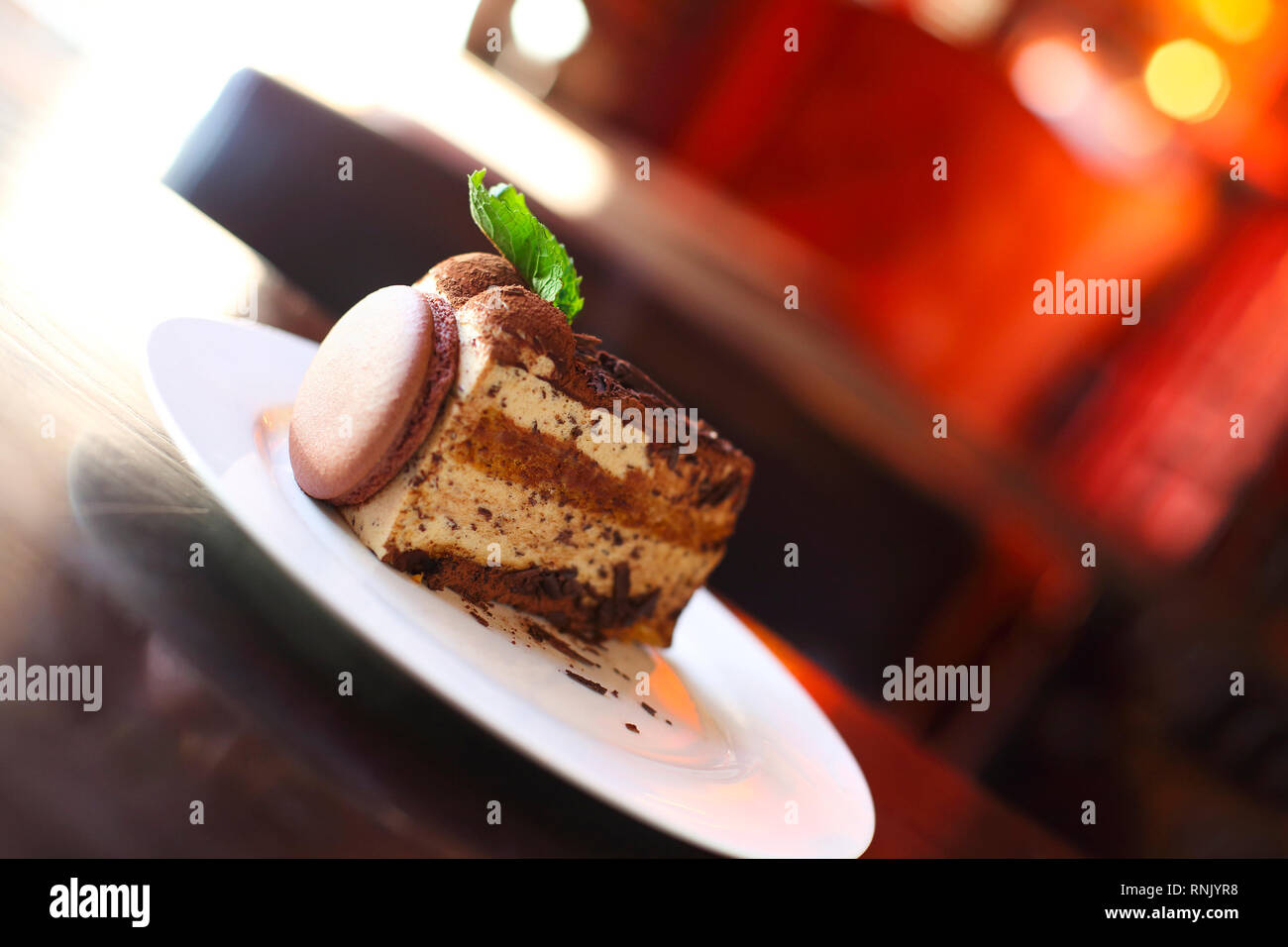 Morceau de gâteau au chocolat décoré de macaron sur plaque blanche, selective focus, arrière-plan lumineux Banque D'Images