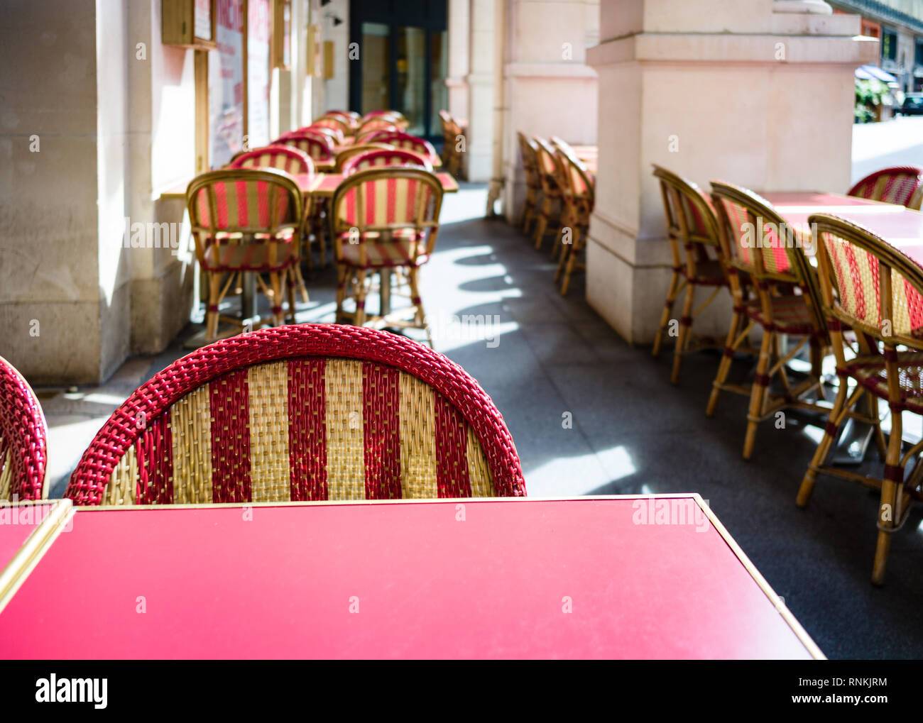 Terrasse typique à l'extérieur d'un café parisien avec la mélamine rouge tables et chaises en rotin sous les arcades au soleil. Banque D'Images