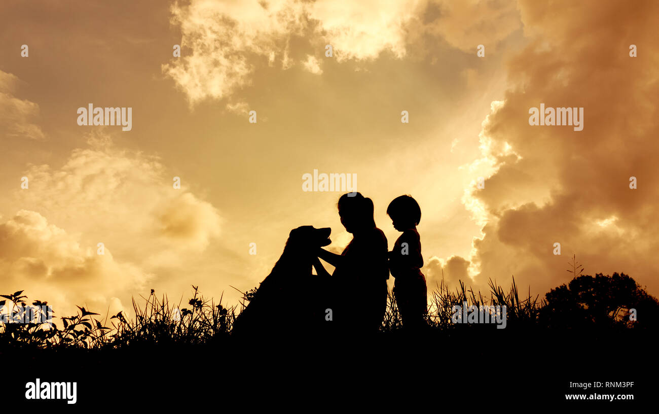 Silhouettes d'une femme avec son enfant et le chien pendant le coucher du soleil Banque D'Images