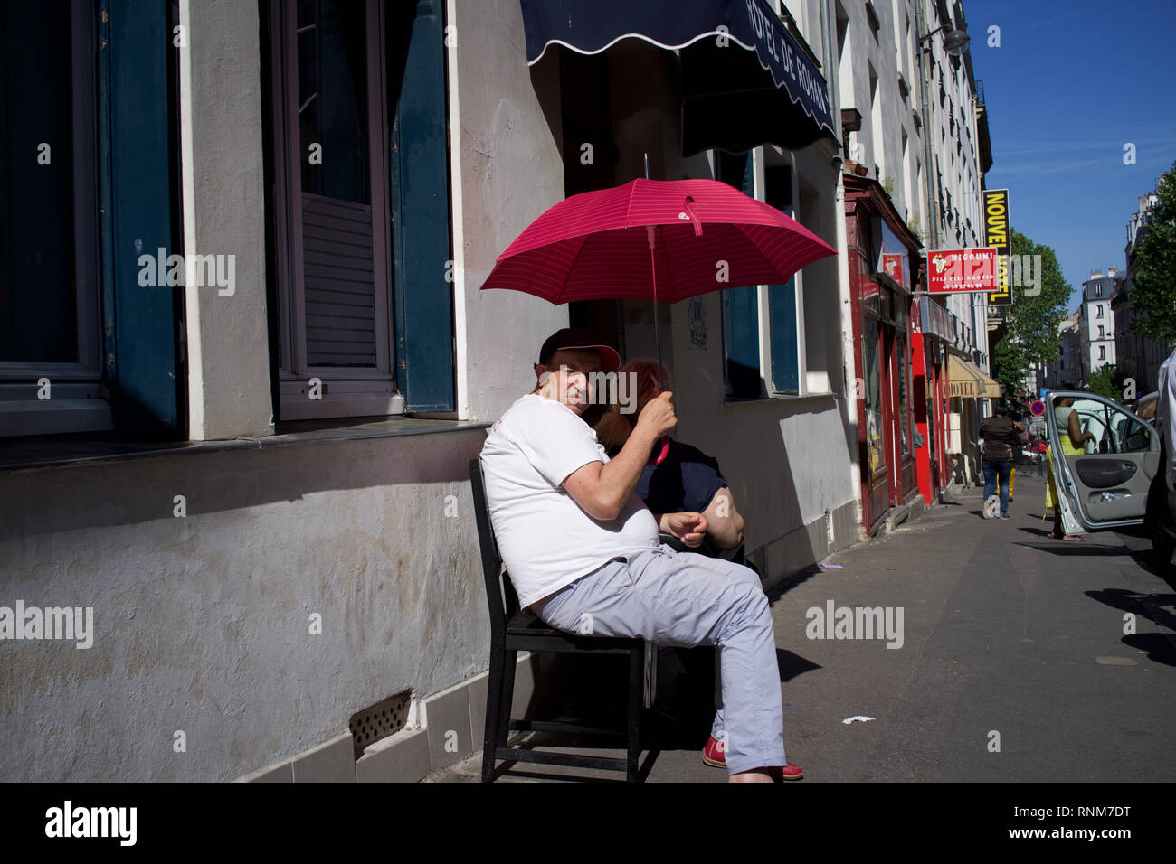Man holding parapluie rouge, l'ombre du soleil lui-même, assis sur des chaises à l'extérieur de l'hôtel Rohan, Rue Myrha, 75018 Paris, France Banque D'Images