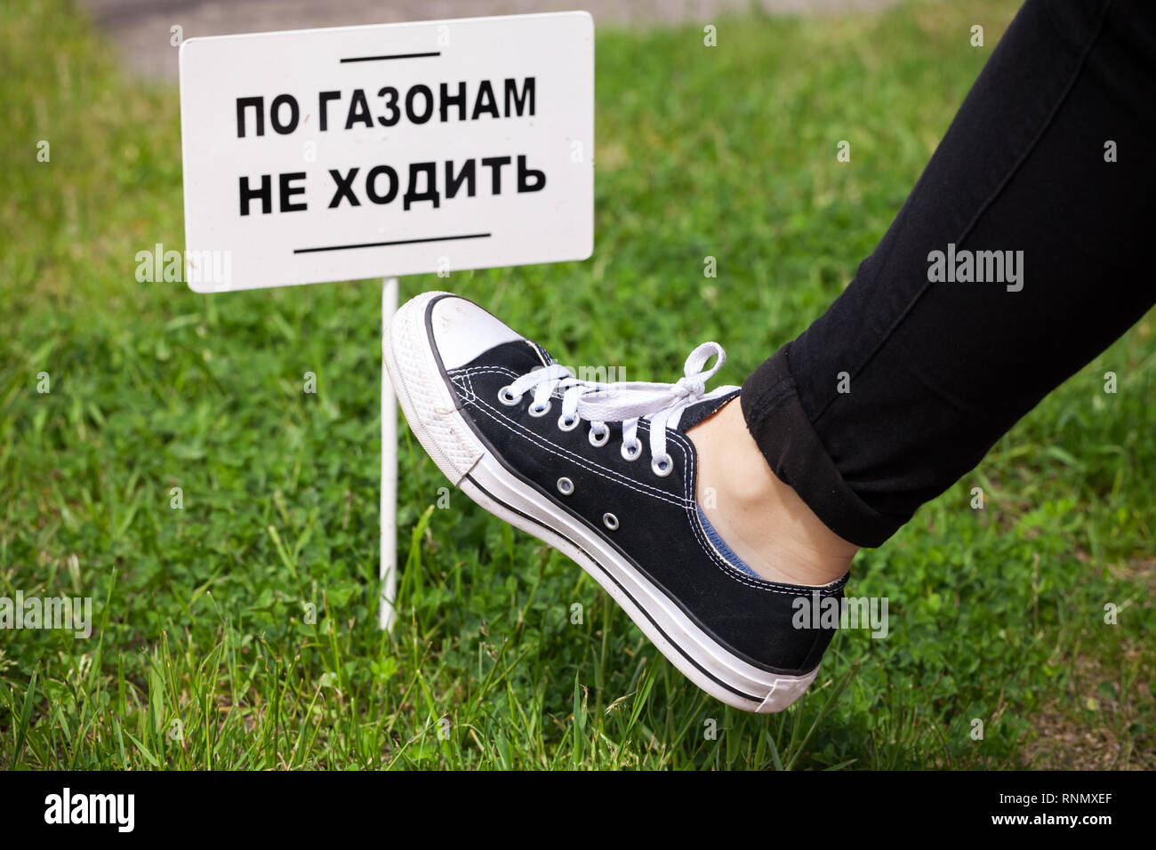 Les adolescents au pied sur l'herbe verte près de petite bannière blanche avec texte russe : Ne pas marcher sur la pelouse ! Banque D'Images