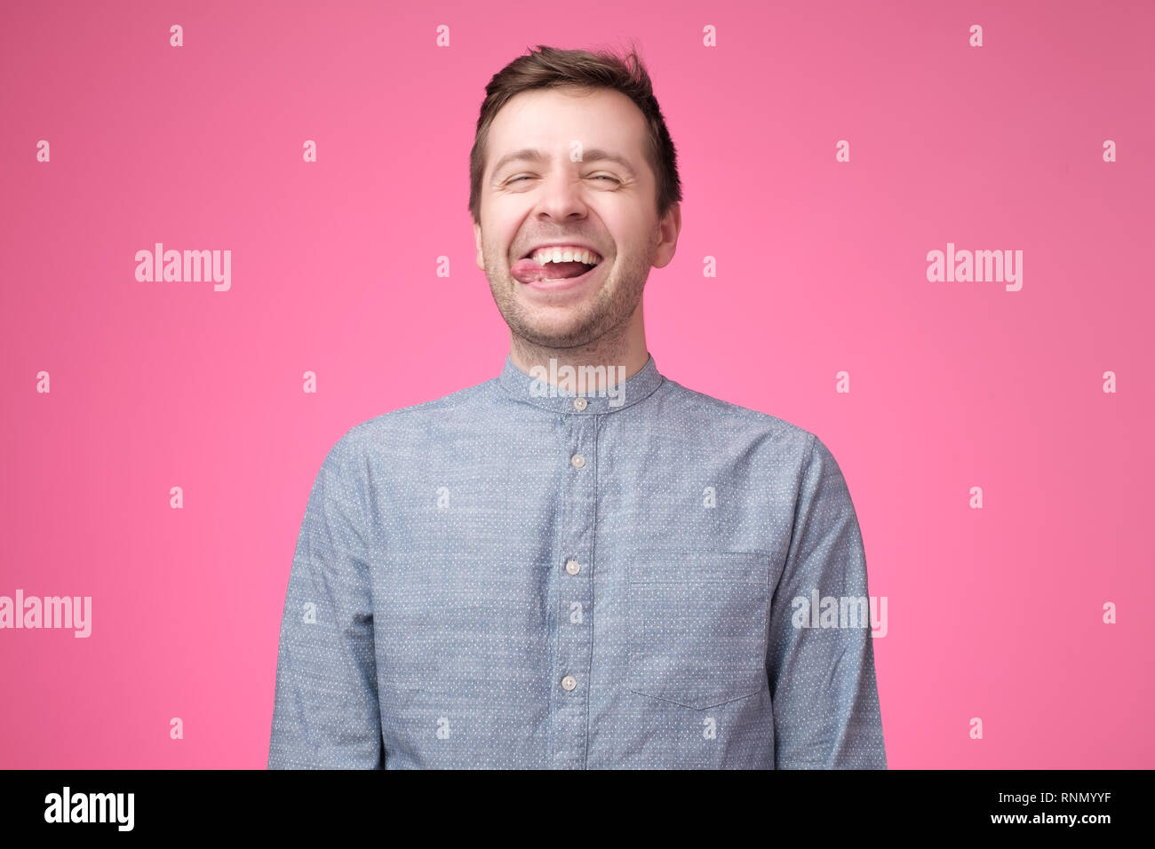 Guy attrayant sans souci en chemise bleue indiquant la langue et faire drôle de visage Banque D'Images