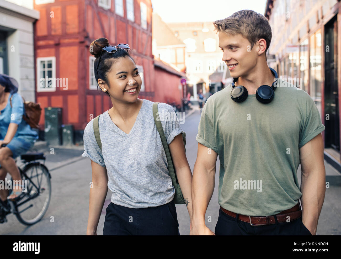 Smiling young woman en marchant main dans la main ensemble le long d'une rue de la ville Banque D'Images