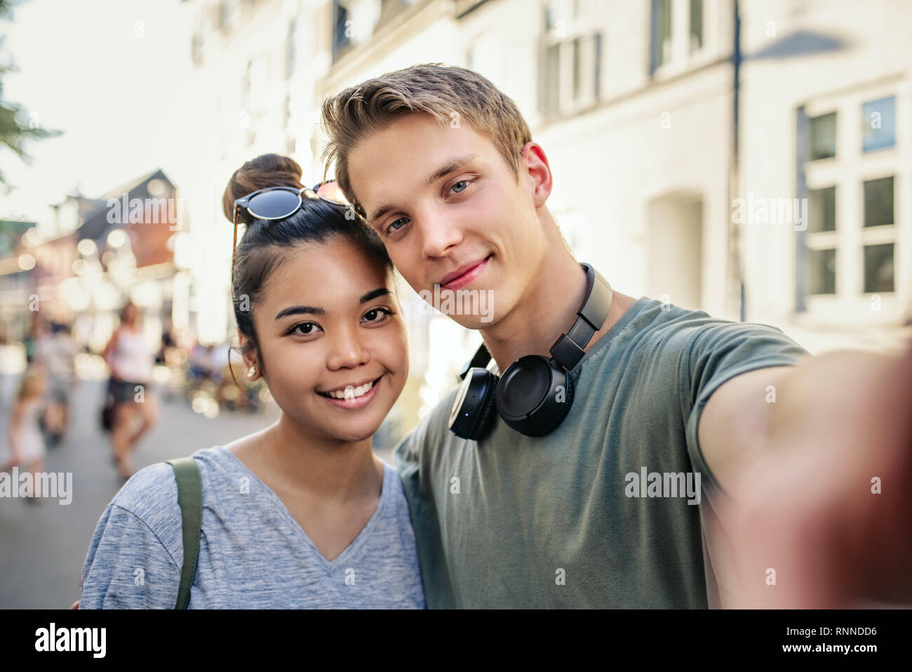 Smiling young couple prenant un ensemble tout en selfies debout dans les bras dans une rue de la ville Banque D'Images