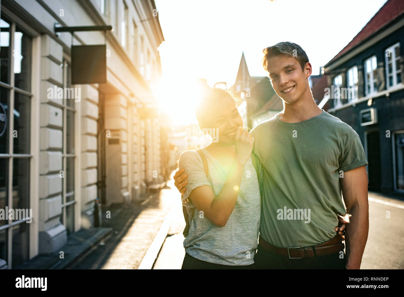 Portrait d'un jeune couple de rire tout en se tenant bras dessus bras dessous ensemble sur une rue de la ville dans l'après-midi Banque D'Images