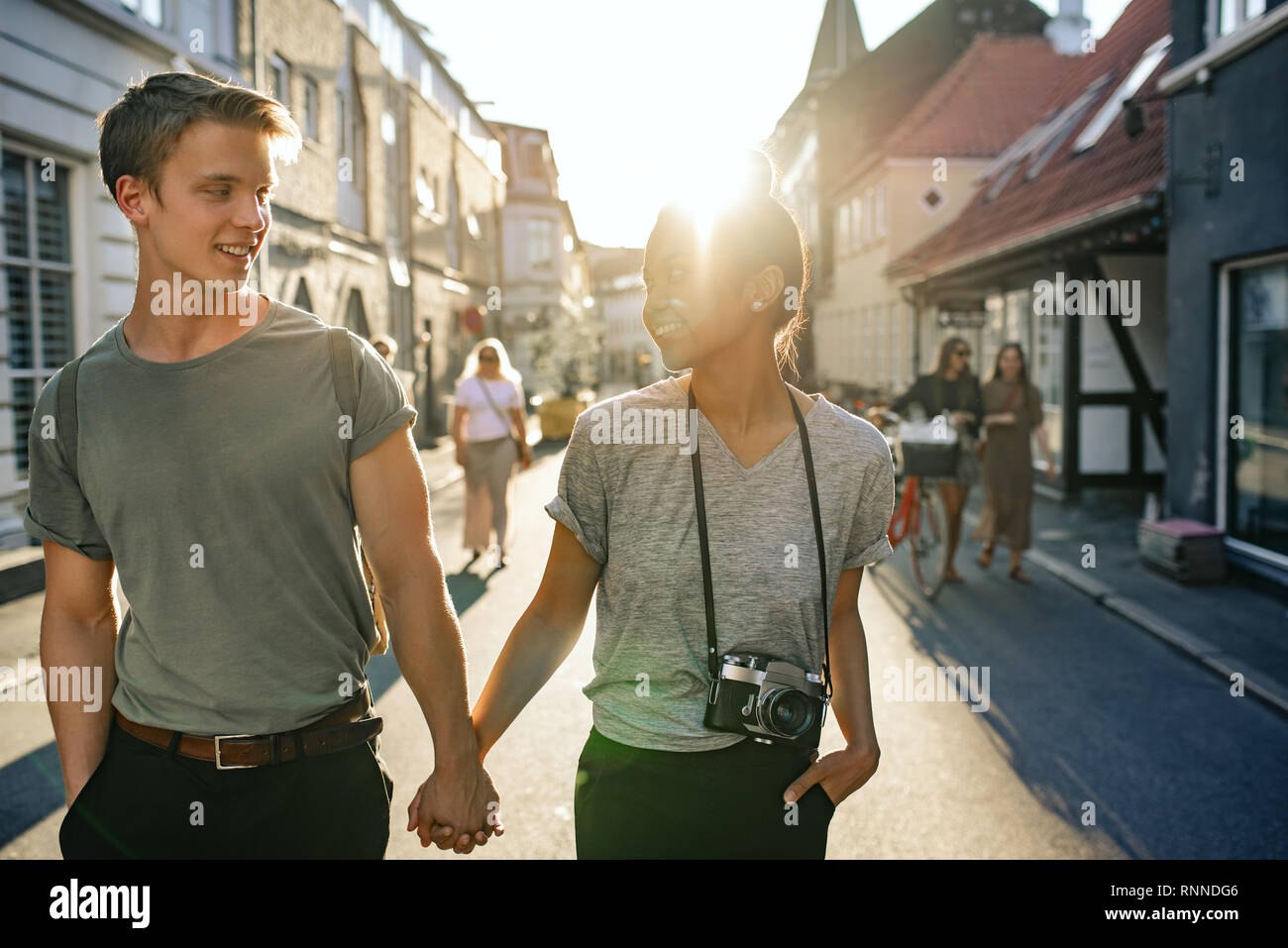 Smiling young couple talking tout en explorant les rues de la ville main dans la main ensemble en fin d'après-midi Banque D'Images