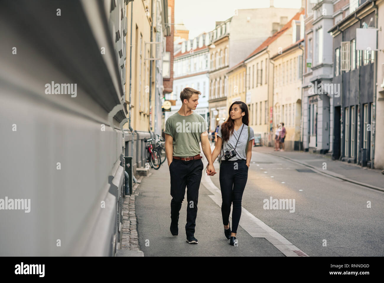 Young couple holding hands et parler ensemble en marchant le long d'un trottoir dans la ville Banque D'Images