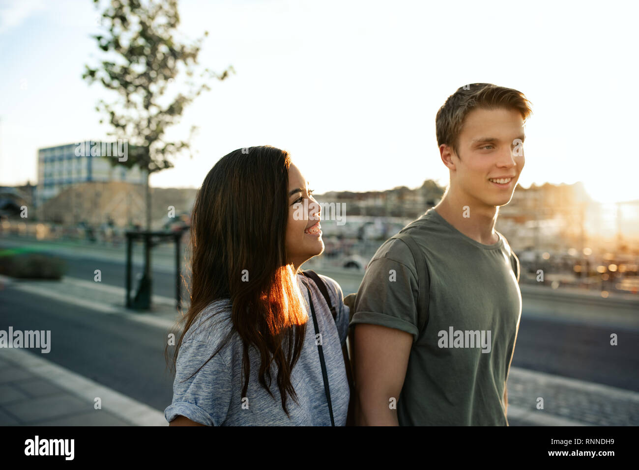 Jeune couple de rire tandis que marcher ensemble le long d'un trottoir dans la ville en fin d'après-midi Banque D'Images