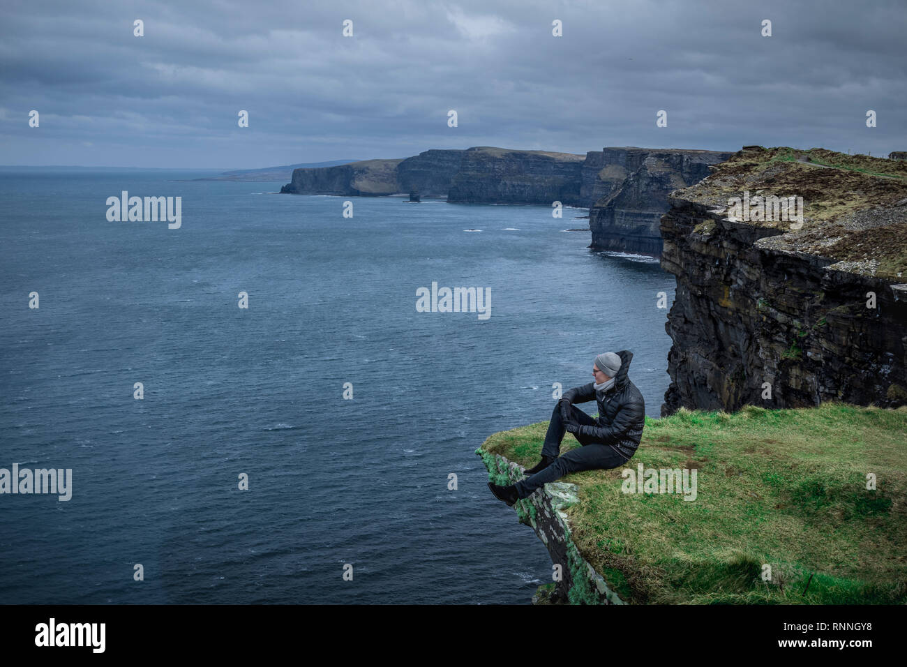 Homme assis sur un rocher avec les Falaises de Moher en arrière-plan Banque D'Images