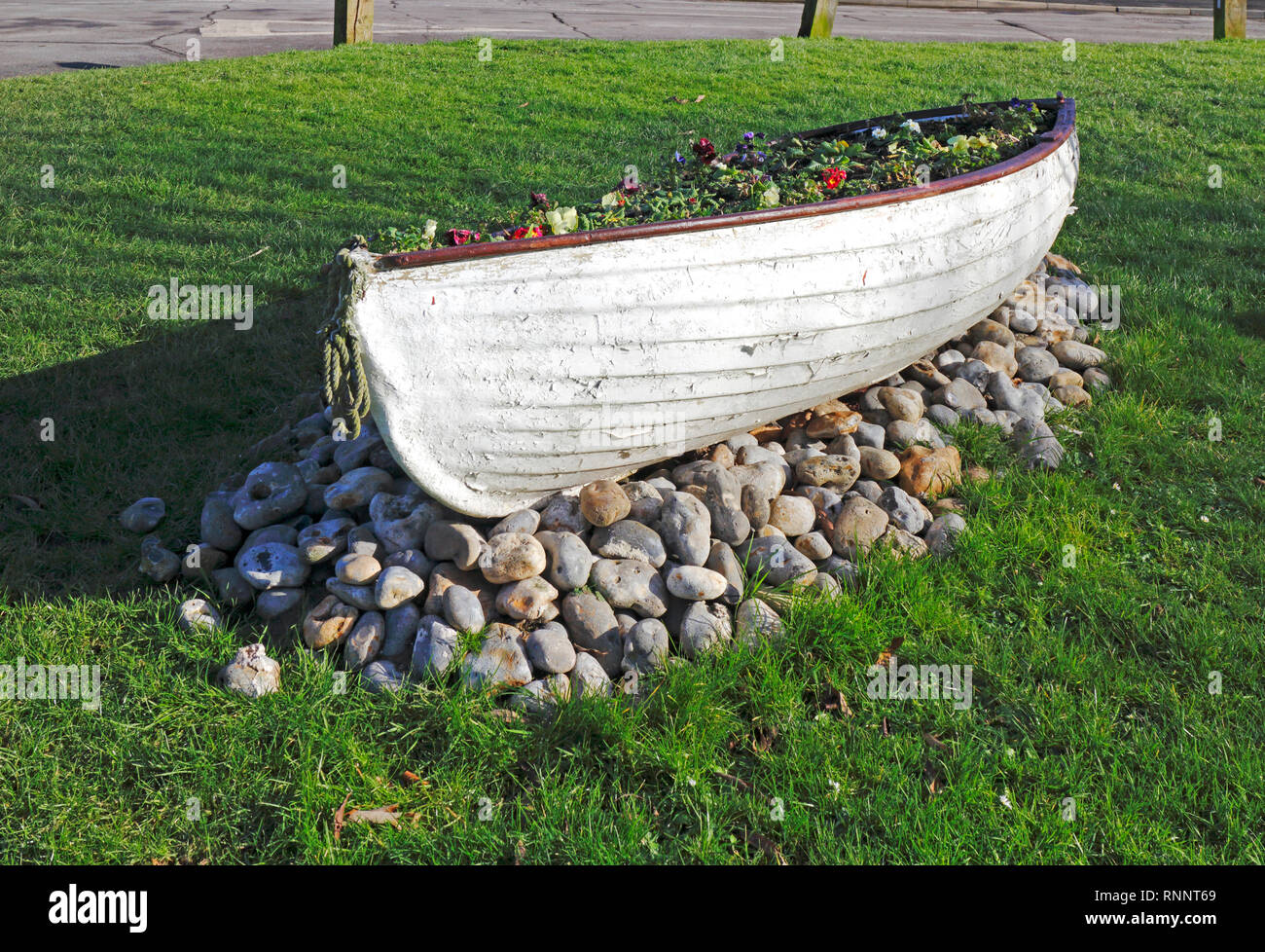 Un canot utilisé comme un parterre de récipient sur le village vert à Winterton-sur-Mer, Norfolk, Angleterre, Royaume-Uni, Europe. Banque D'Images