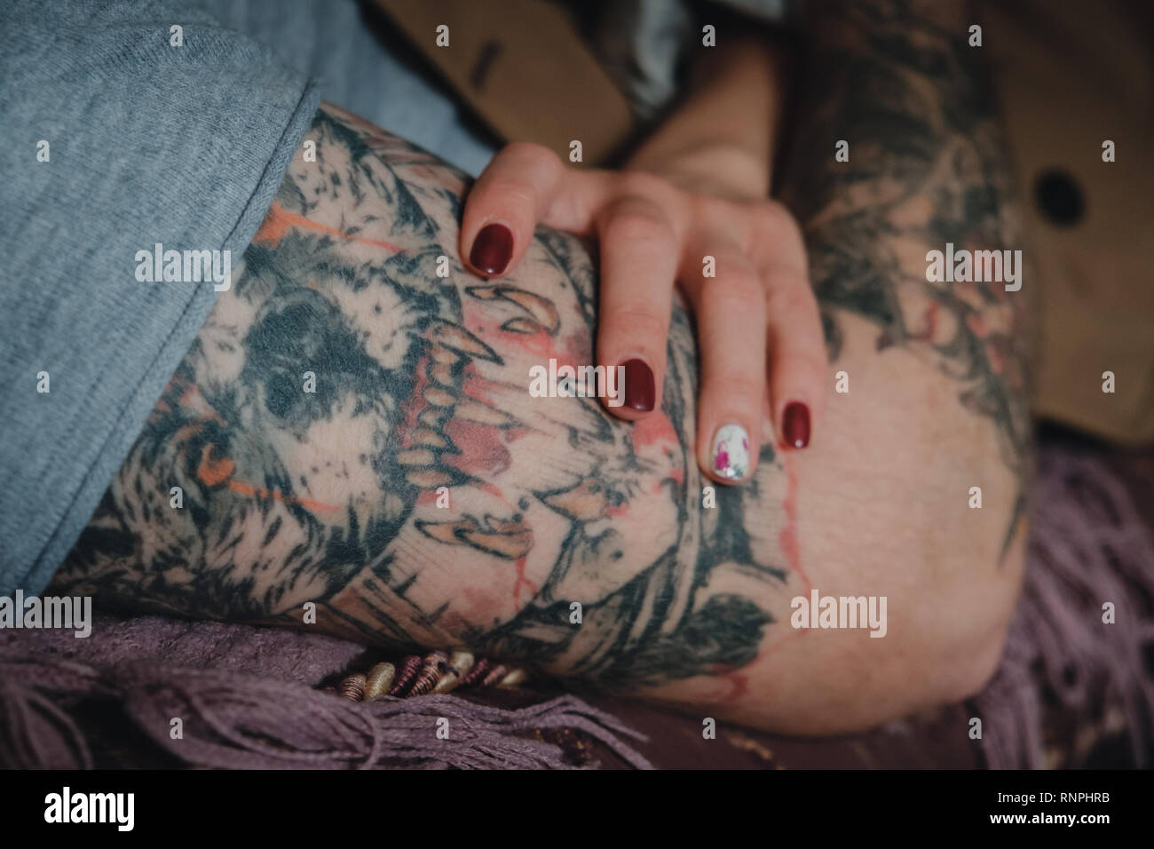 Gros plan d'une main de femme tendre avec red nails polish tenant un homme fort la main avec un manchon tattoo scarry. Banque D'Images