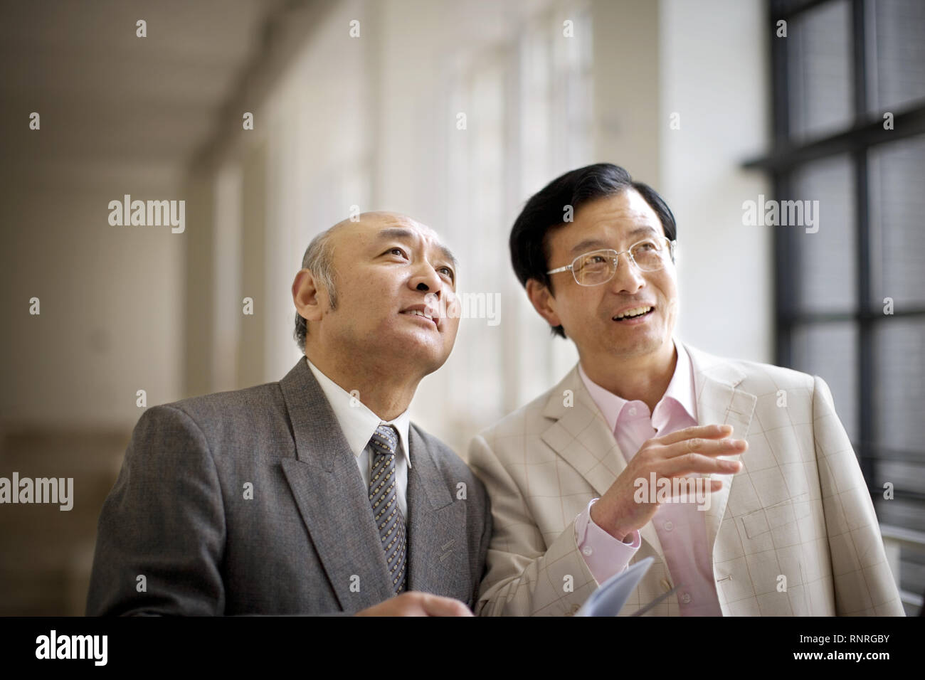 Mid-adult male teacher marcher avec un collègue masculin senior dans une salle. Banque D'Images