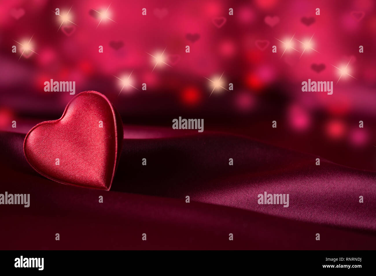 Coeur rouge isolé couché sur le côté sur satin violet - coeurs délicats et taches bokeh et stars Banque D'Images