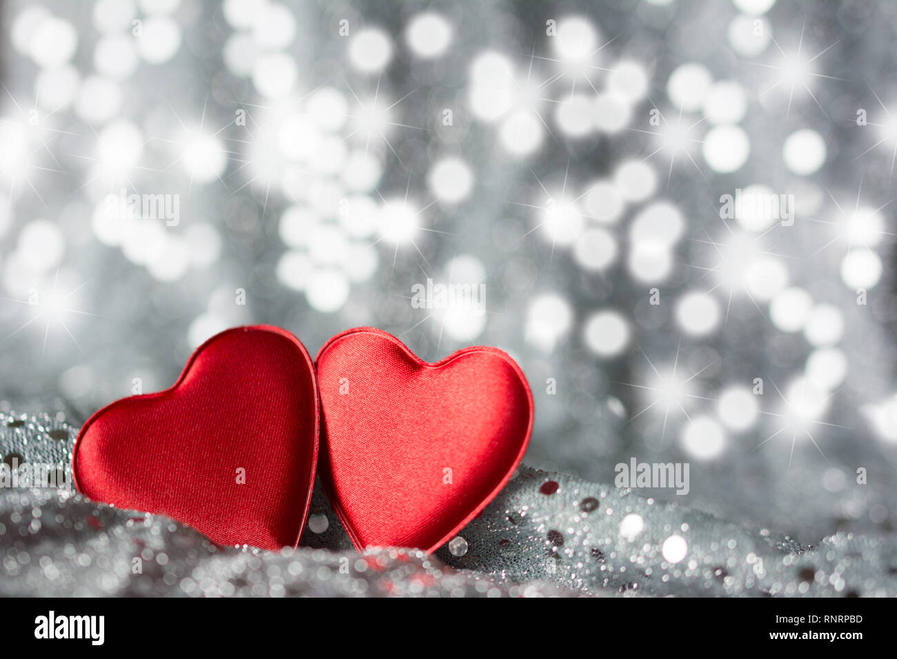 Deux coeurs rouges sur tissu avec paillettes argent - fond argenté avec étoile et taches bokeh Banque D'Images