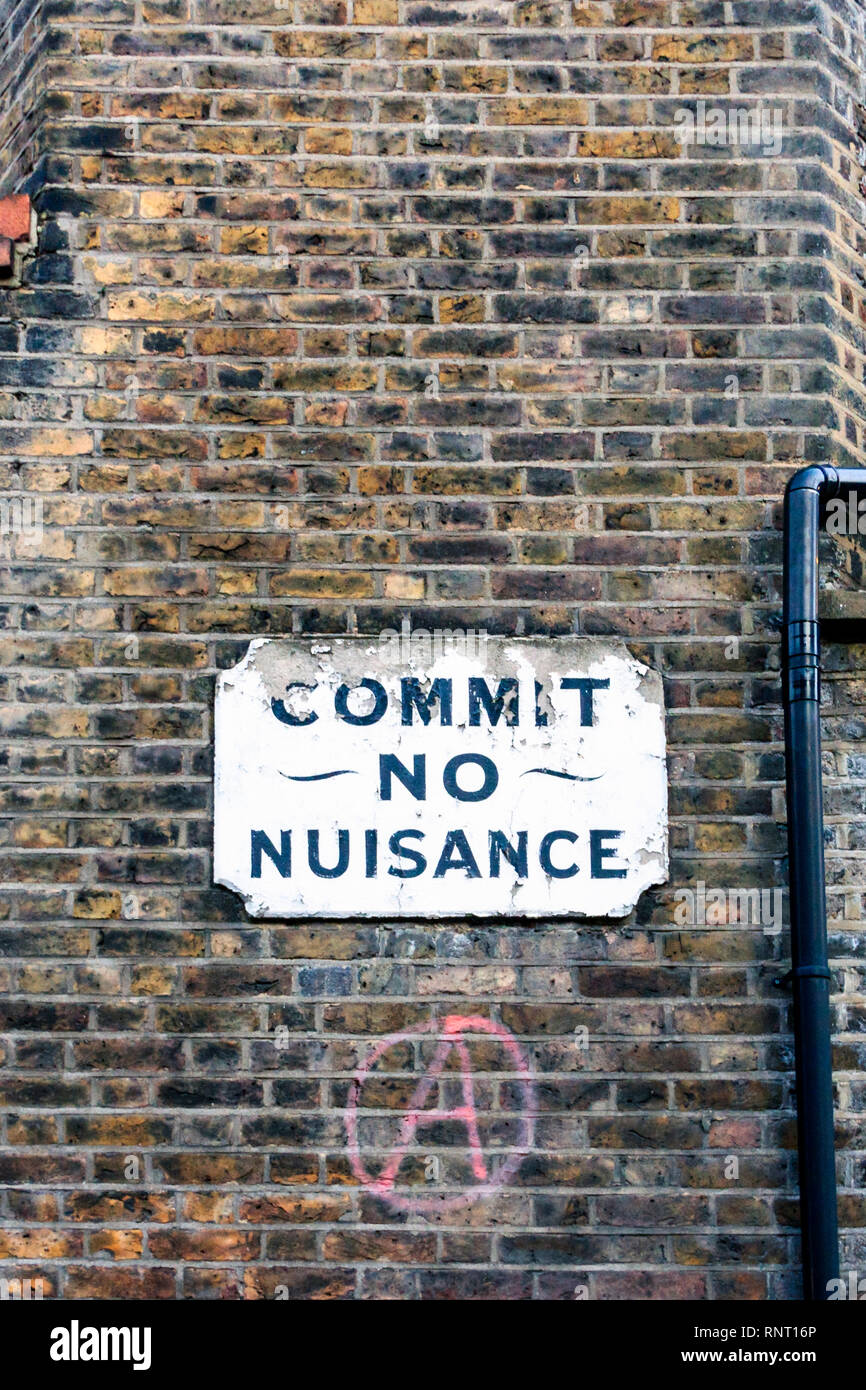 Un vieux panneau 'Commit aucune nuisance', ci-dessous un signe anarchie peint en rouge, sur le mur de brique d'un immeuble en bloc de Southwark, Londres, UK Banque D'Images