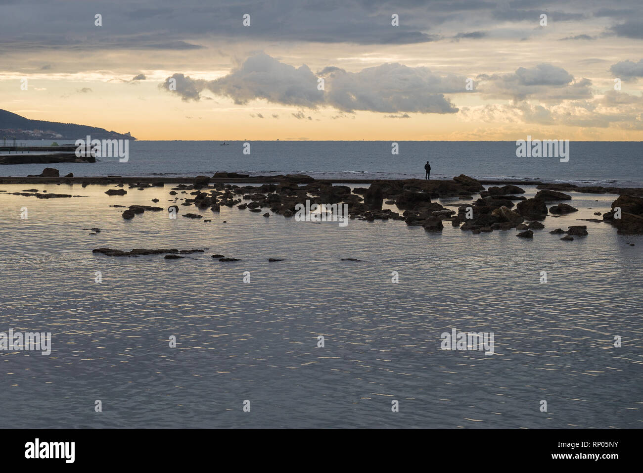 Homme debout sur des rochers au milieu de la mer regardant cargos, ciel nuageux. Banque D'Images