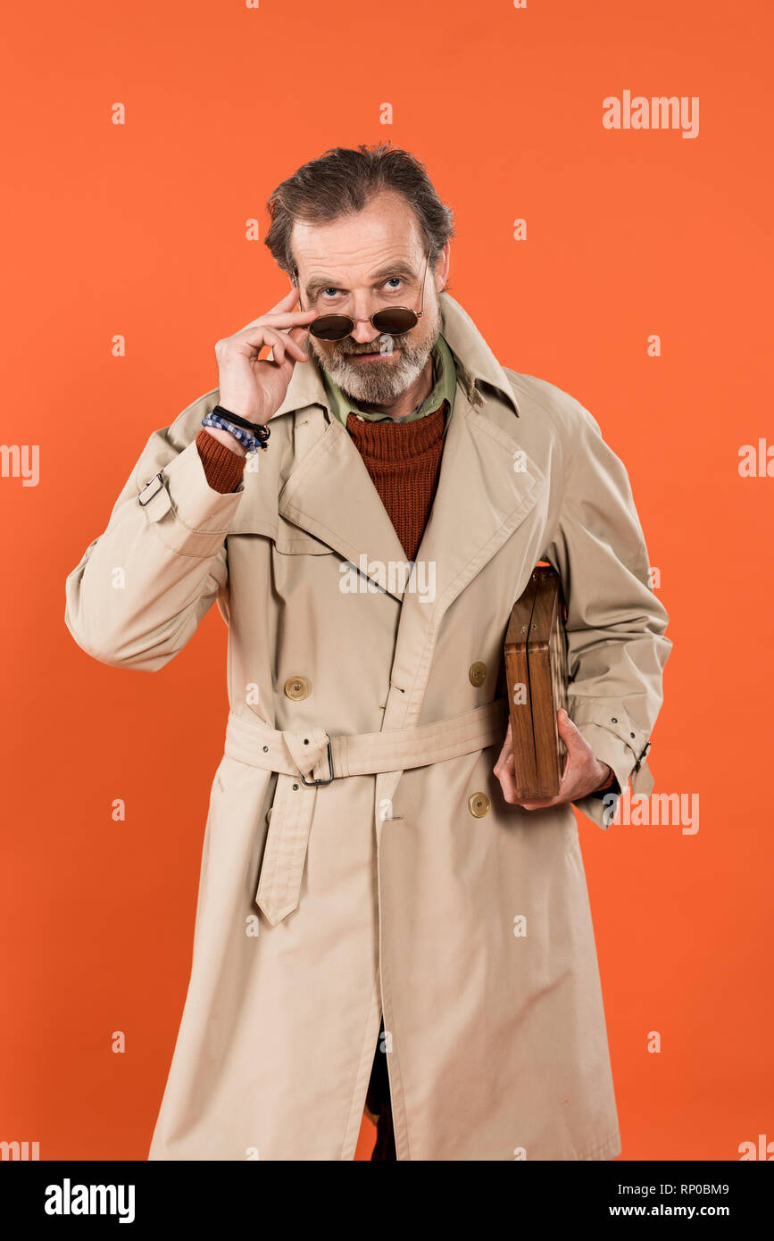 Trendy man lunettes de toucher tout en se tenant à l'échiquier isolé sur orange Banque D'Images