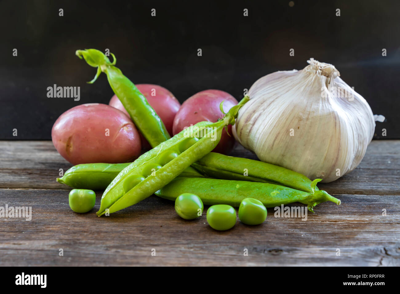 Les pommes de terre, chef de l'ail et les gousses de pois sur une planche en bois close up Banque D'Images