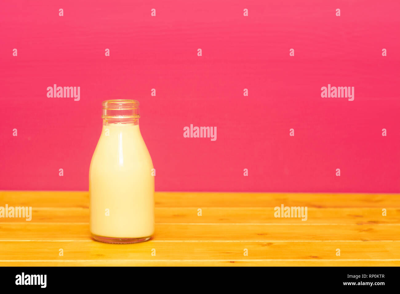 Milkshake banane dans une troisième pinte de lait, bouteille en verre sur une table en bois contre un arrière-plan peint rose Banque D'Images