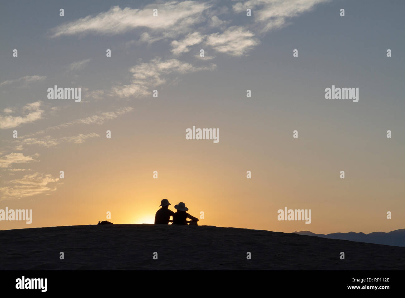 Un couple assis sur une dune de sable au coucher du soleil découpé sur le soleil, Mesquite Flat dunes de sable, la Death Valley National Park, California, United States Banque D'Images