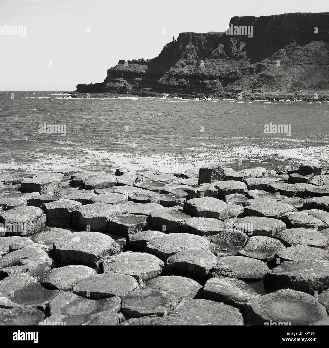 Années 1950, tableau historique montrant l'ancienne colonnes de basalte hexagonales entrelacées ou des pierres sur le bord de mer à la Giant's Causeway, situé sur les côtes de l'Atlantique Nord, l'Irlande du Nord, Royaume-Uni. Banque D'Images