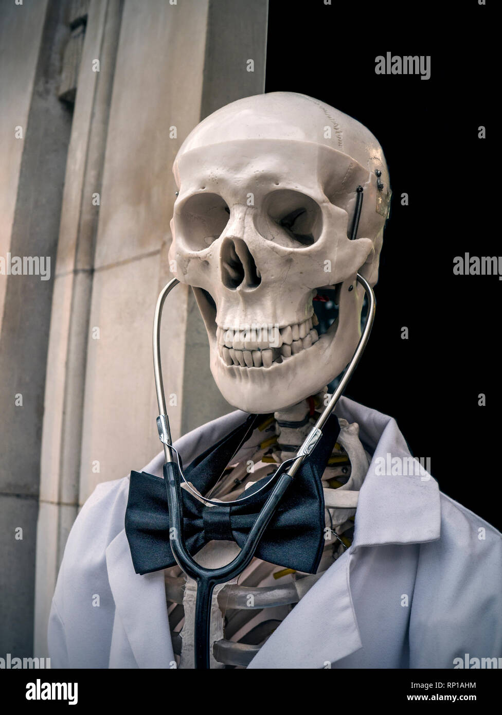 Dr DEATH CONCEPT MÉDICAL NHS LISTE D'ATTENTE skull squelette souriant vêtu  de médecins manteau blanc et noeud papillon avec stéthoscope agissant comme  un 'Doctor Death'.Un rappel humoristique à l'extérieur d'un établissement  médical