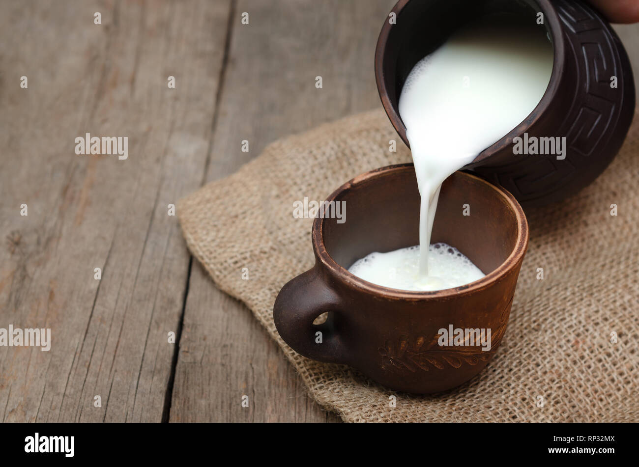 Verser le lait frais dans une tasse d'argile sur fond de bois. Banque D'Images