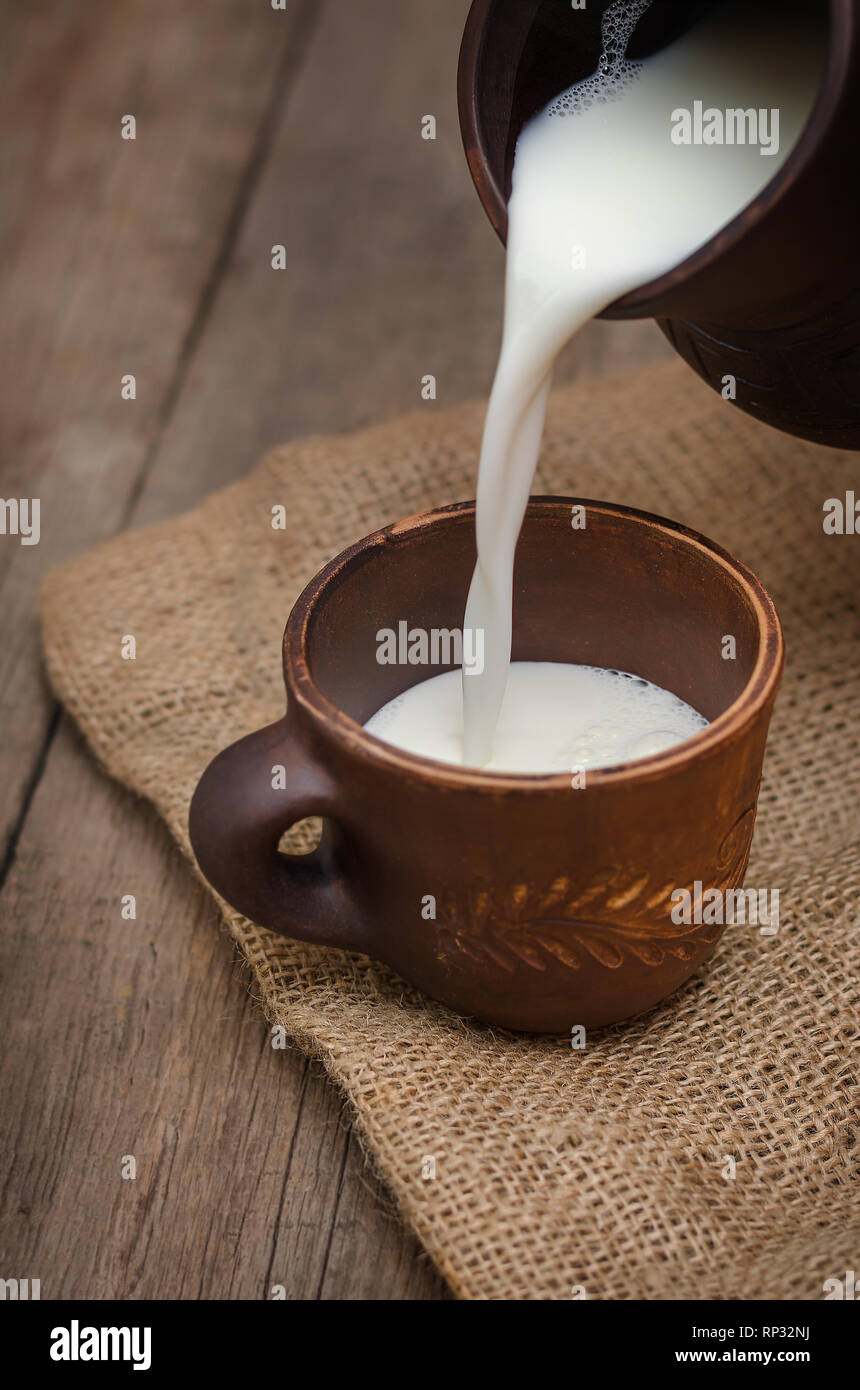 Verser le lait frais dans une tasse d'argile sur fond de bois. Banque D'Images