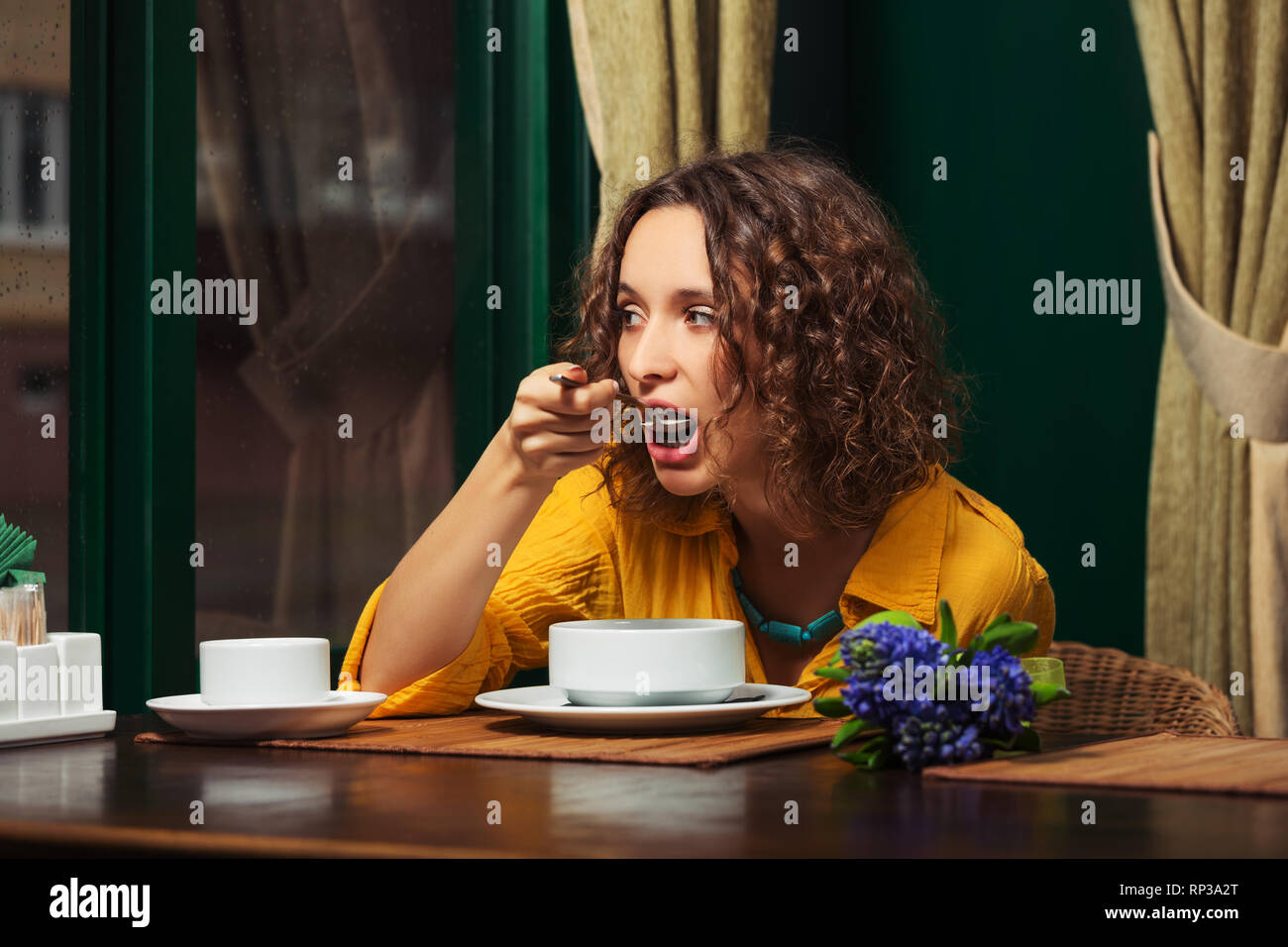 Jeune femme de manger une soupe à l'élégant restaurant fashion model avec brown poils frisés portant chemise jaune Banque D'Images