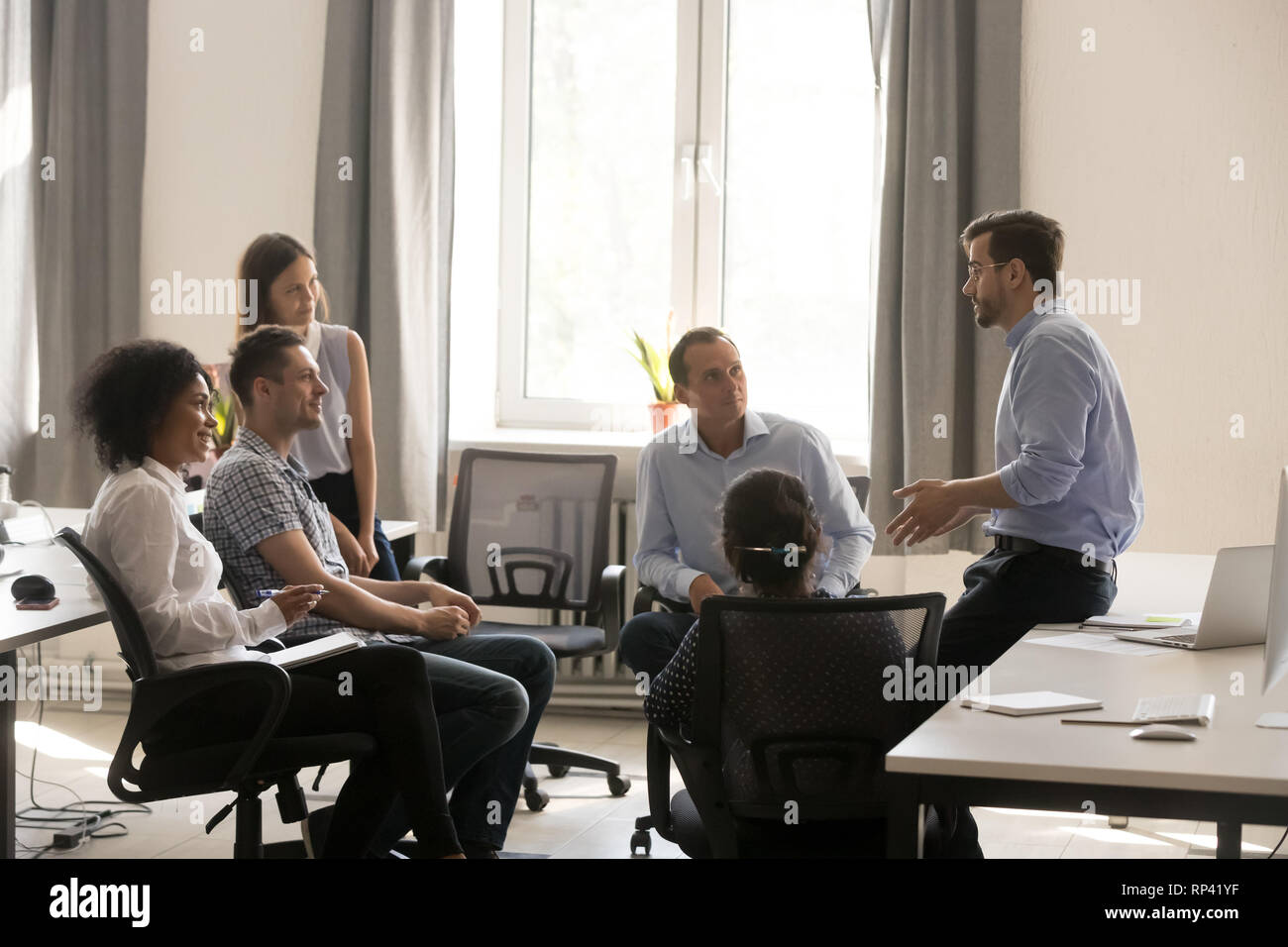 L'équipe de créatifs multiraciale divers travailleurs millénaire écouter leader ou propriétaire de l'entreprise à répondre à l'espace de coworking. Les gens au remue-méninges se d Banque D'Images