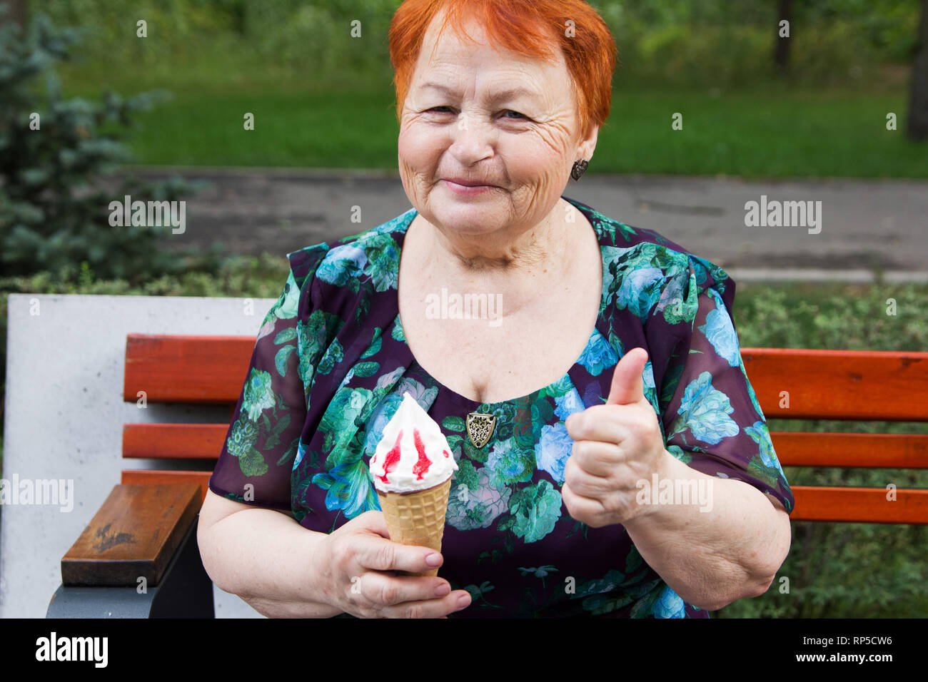 Femme âgée avec de la crème glacée est assis sur un banc dans le parc en été Banque D'Images