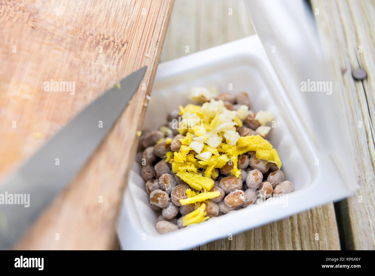 Gros plan du natto japonais asiatique plat de soja fermenté contenant en styromousse repas au Japon fort et le couteau planche à hacher l'ail et le gingembre sur ma table en bois Banque D'Images