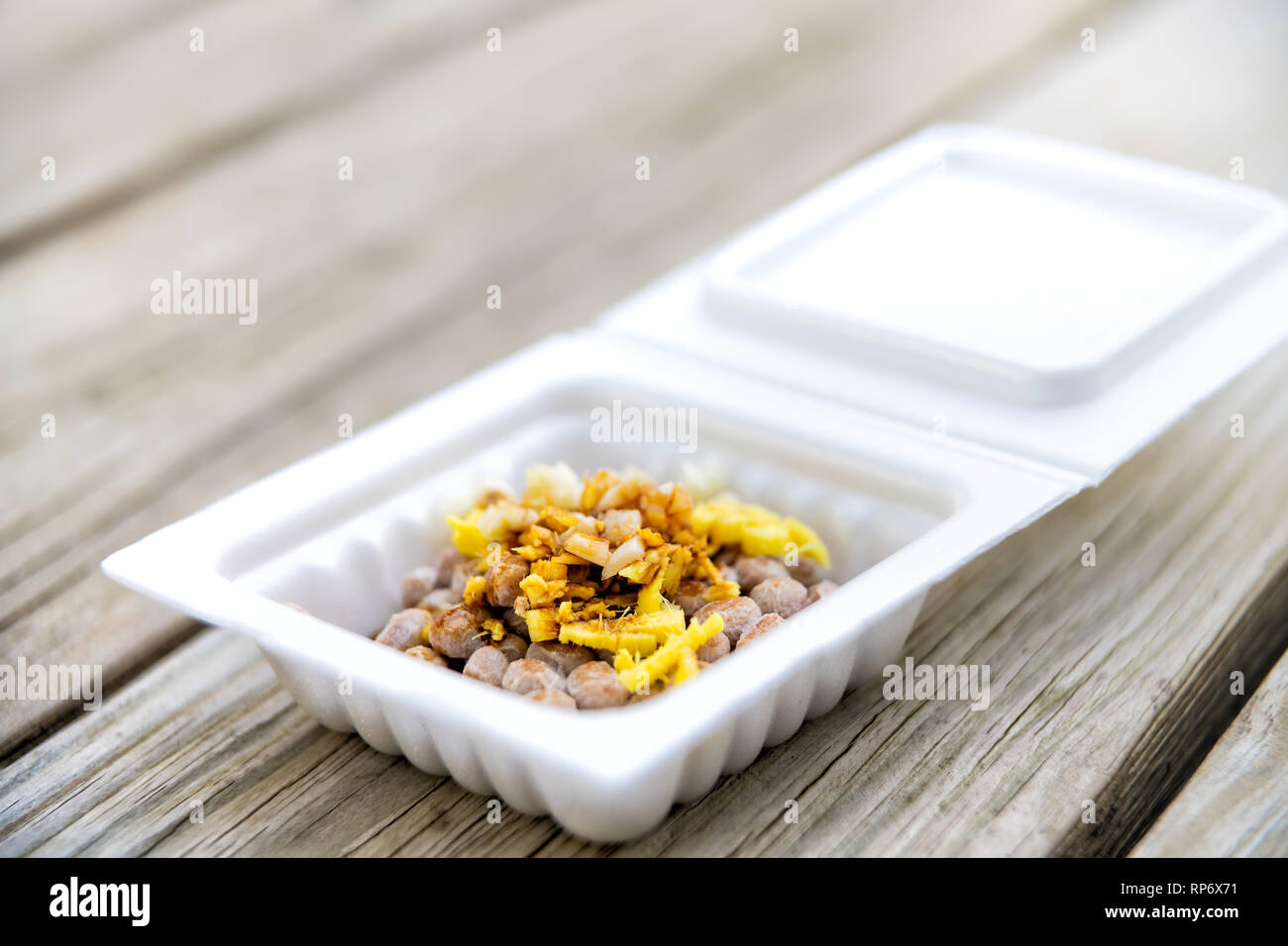 Gros plan du natto japonais asiatique plat de soja fermenté contenant en styromousse repas au Japon fort et garnitures sauce soja ail et le gingembre sur table en bois amrc Banque D'Images