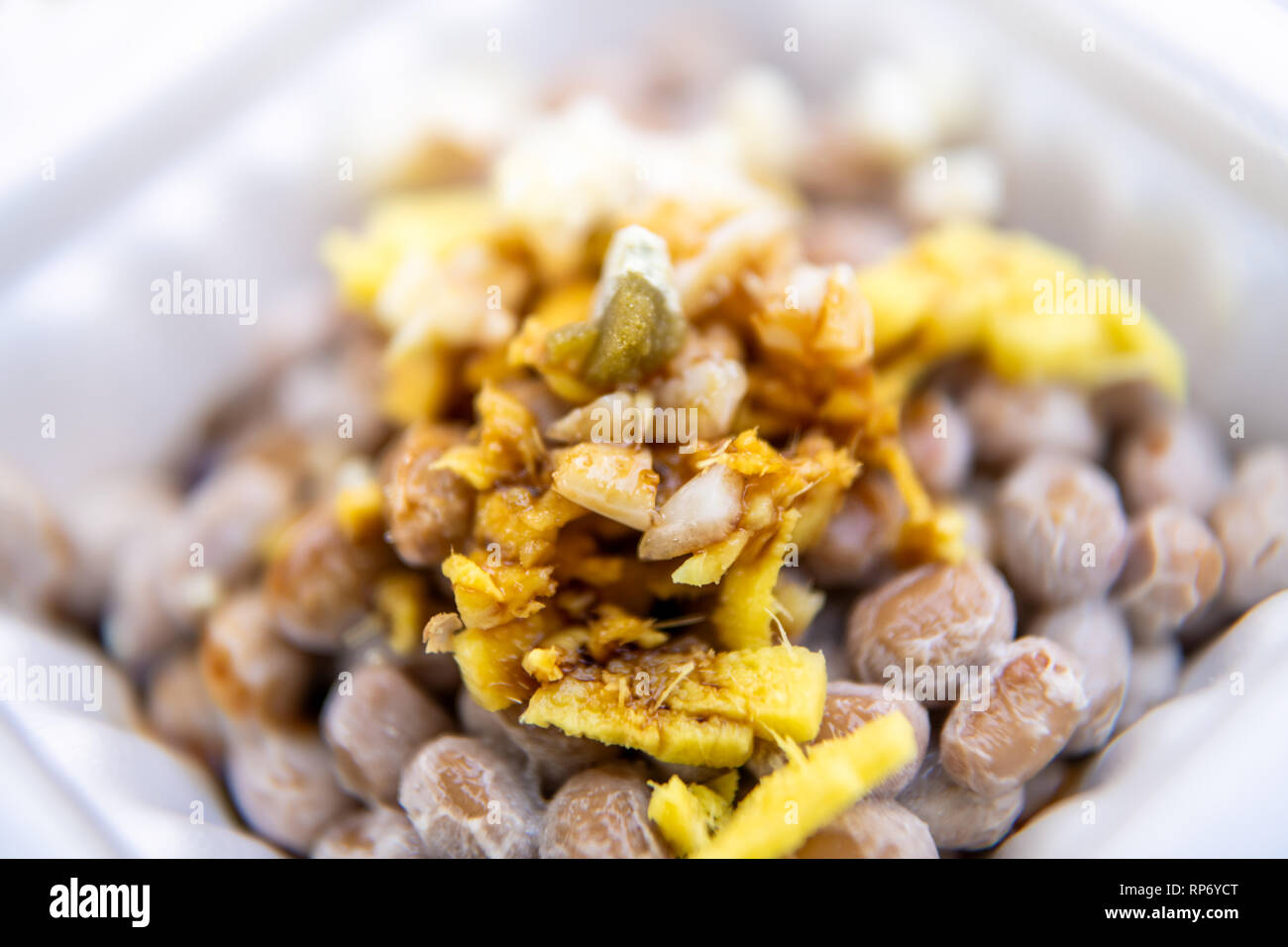 Gros plan macro de natto japonais asiatique plat de soja fermenté contenant en styromousse repas au Japon fort et garnitures sauce soja ail et gingembre Banque D'Images
