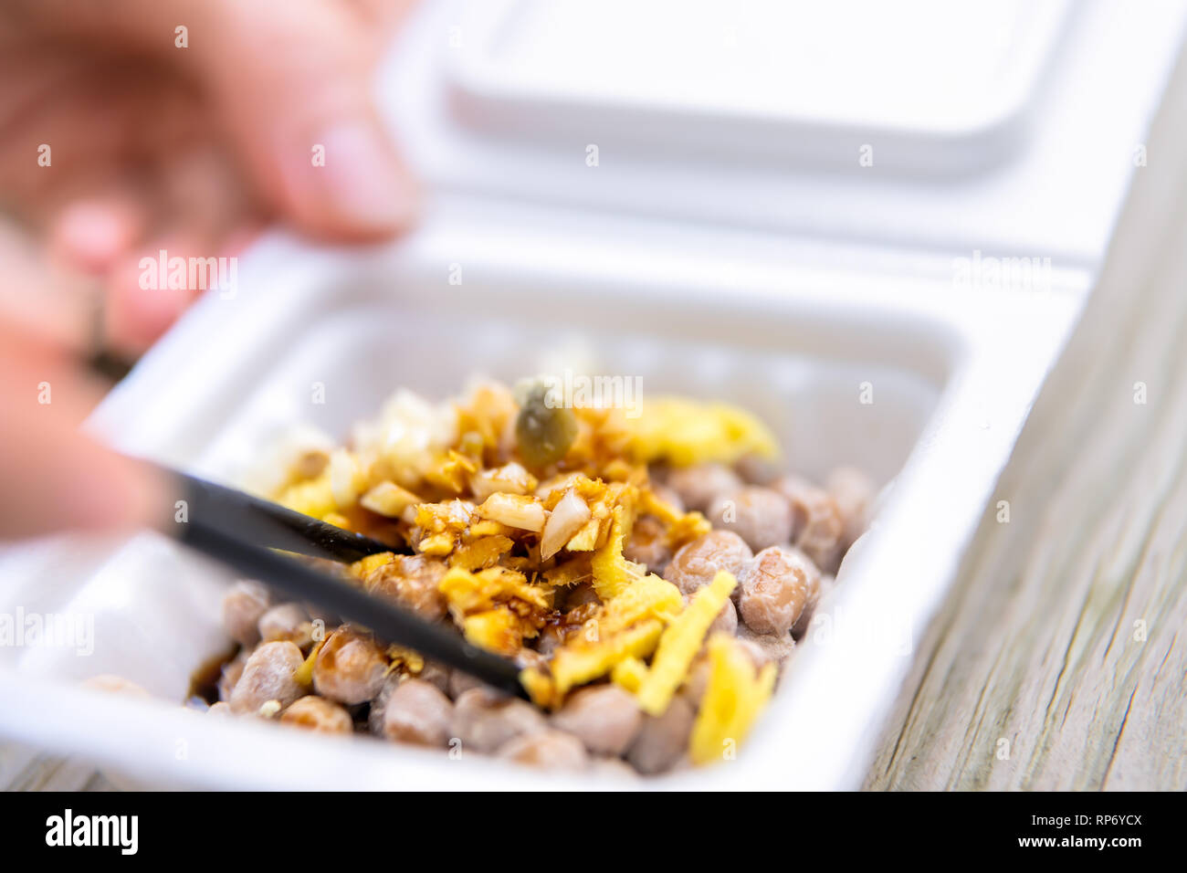 Gros plan macro de natto japonais asiatique plat de soja fermenté contenant en styromousse repas au Japon fort et baguettes garnitures sauce soja mélange mains g ail Banque D'Images