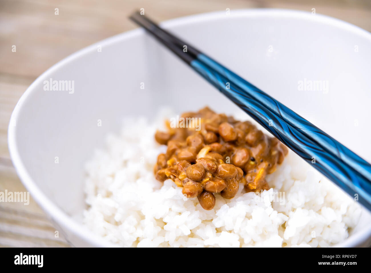 Macro closeup on Blue chopsticks natto japonais asiatique plat de soja fermenté en texture visqueuse collante de repas blanc ordinaire dans un bol de riz cuit à la vapeur Banque D'Images