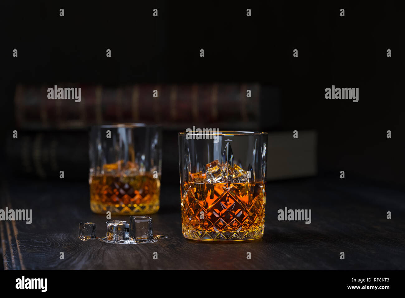Deux verres de whisky avec de la glace, de se tenir sur une vieille table en bois foncé avec de vieux livres sur un fond noir Banque D'Images
