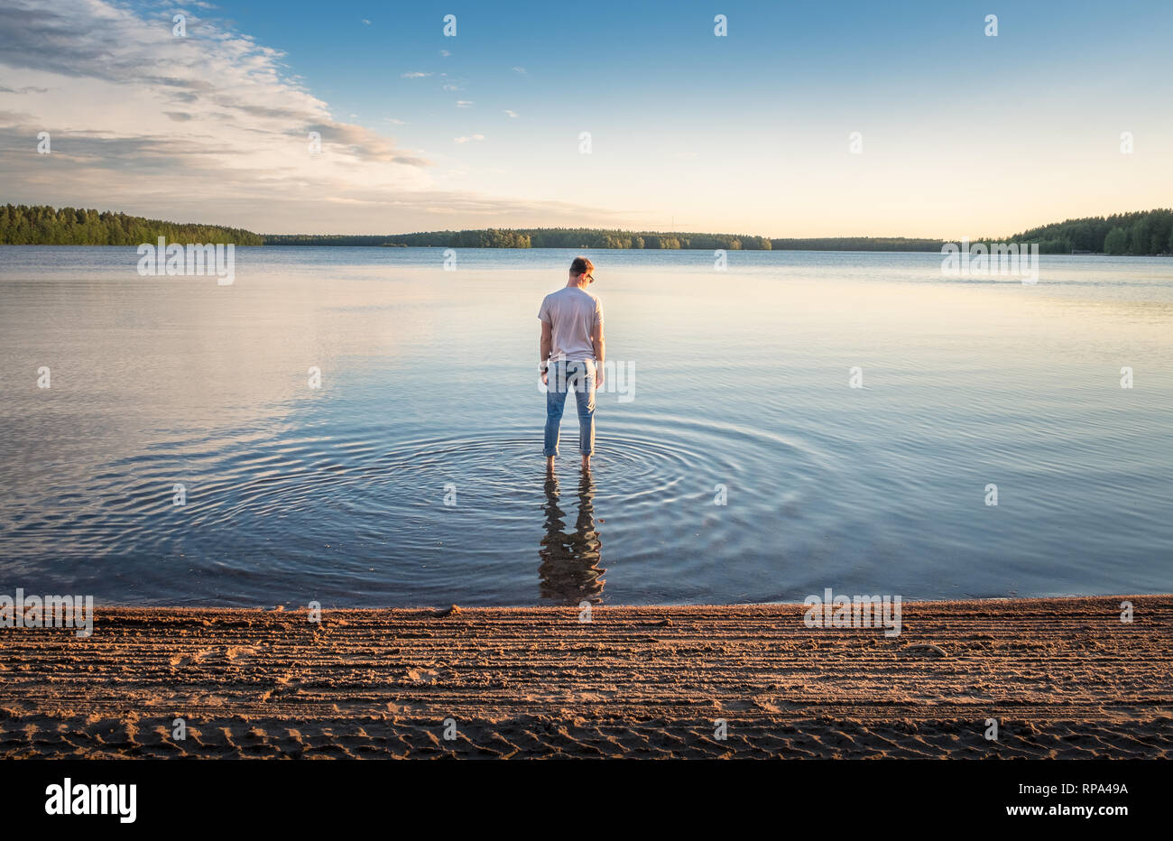 Homme debout dans l'eau à une belle journée d'été avec lac idyllique et paisible soirée en Finlande Banque D'Images