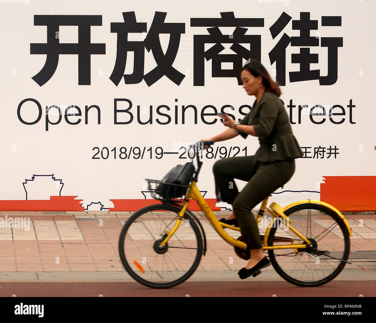 Beijing, Chine. 19 Sep, 2018. Une femme chinoise cours des cycles une entreprise commerciale internationale ouverte street à Pékin le 19 septembre 2018. La Chine a annoncé cette semaine les tarifs douaniers sur les marchandises des États-Unis d'une valeur de 60 milliards de dollars en représailles à la décision du Président Donald Trump d'imposer des droits sur 200 milliards de produits chinois que la guerre commerciale entre les deux plus grandes économies du monde s'intensifie. Credit : Todd Lee/ZUMAprilESS.com/ZUMA Wire/Alamy Live News Banque D'Images