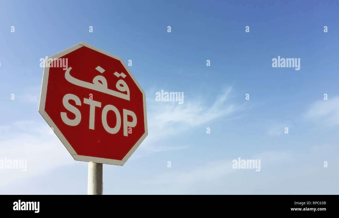 Un panneau d'avertissement stop octogonal rouge avec texte arabe contre le ciel bleu Banque D'Images