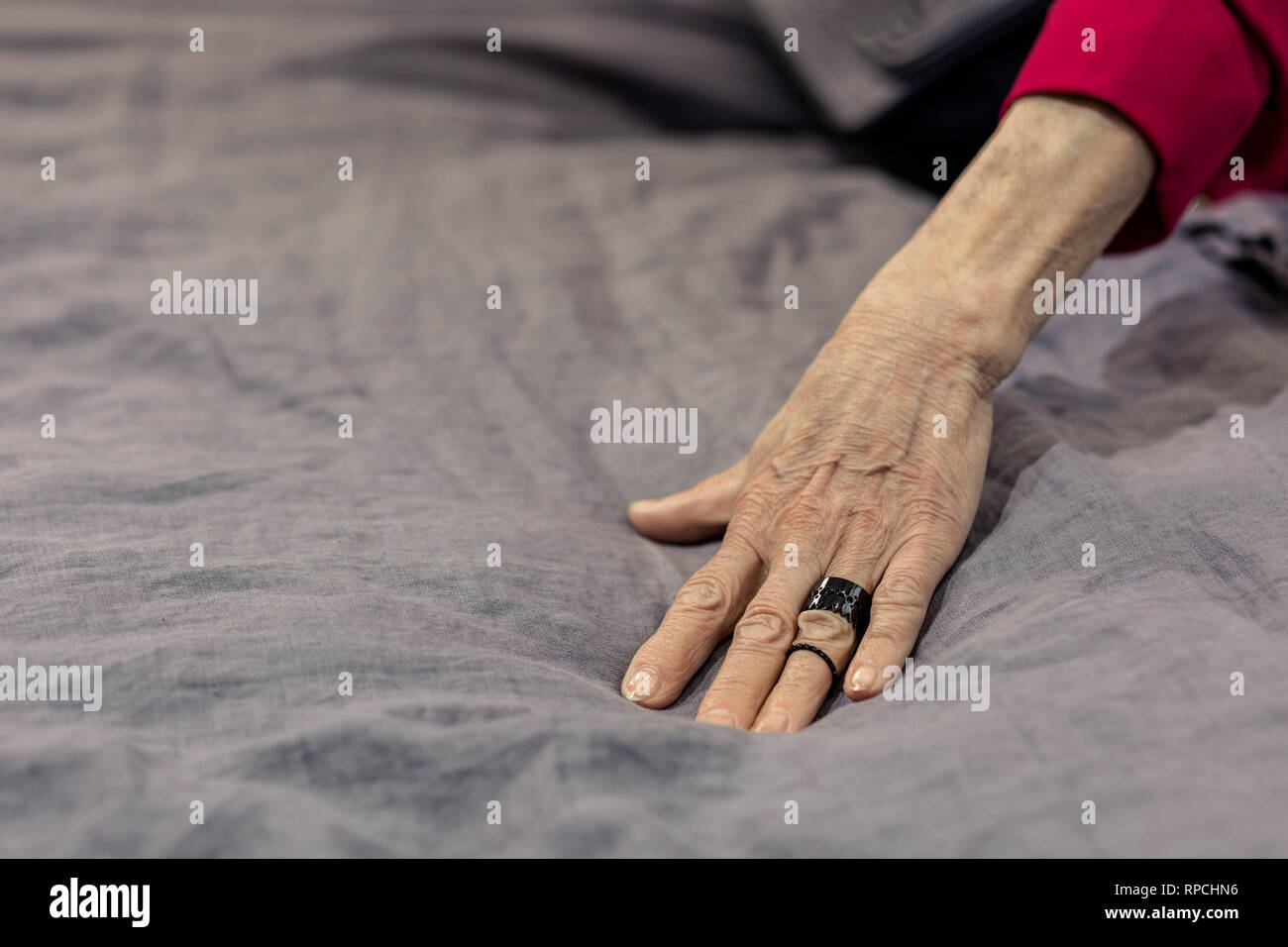 Mug shot du vieillissement madame la main sur lit de draps gris Banque D'Images