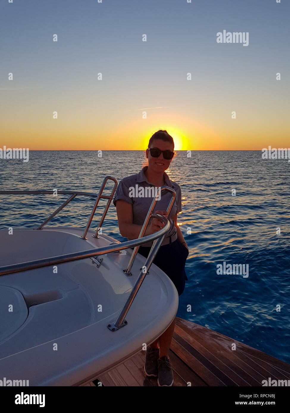 Portriat d'une jeune femme normale à hôtesse de l'au coucher du soleil dans la poupe d'un bateau super en haute mer. Bahamas. Le port de lunettes et souriant Banque D'Images