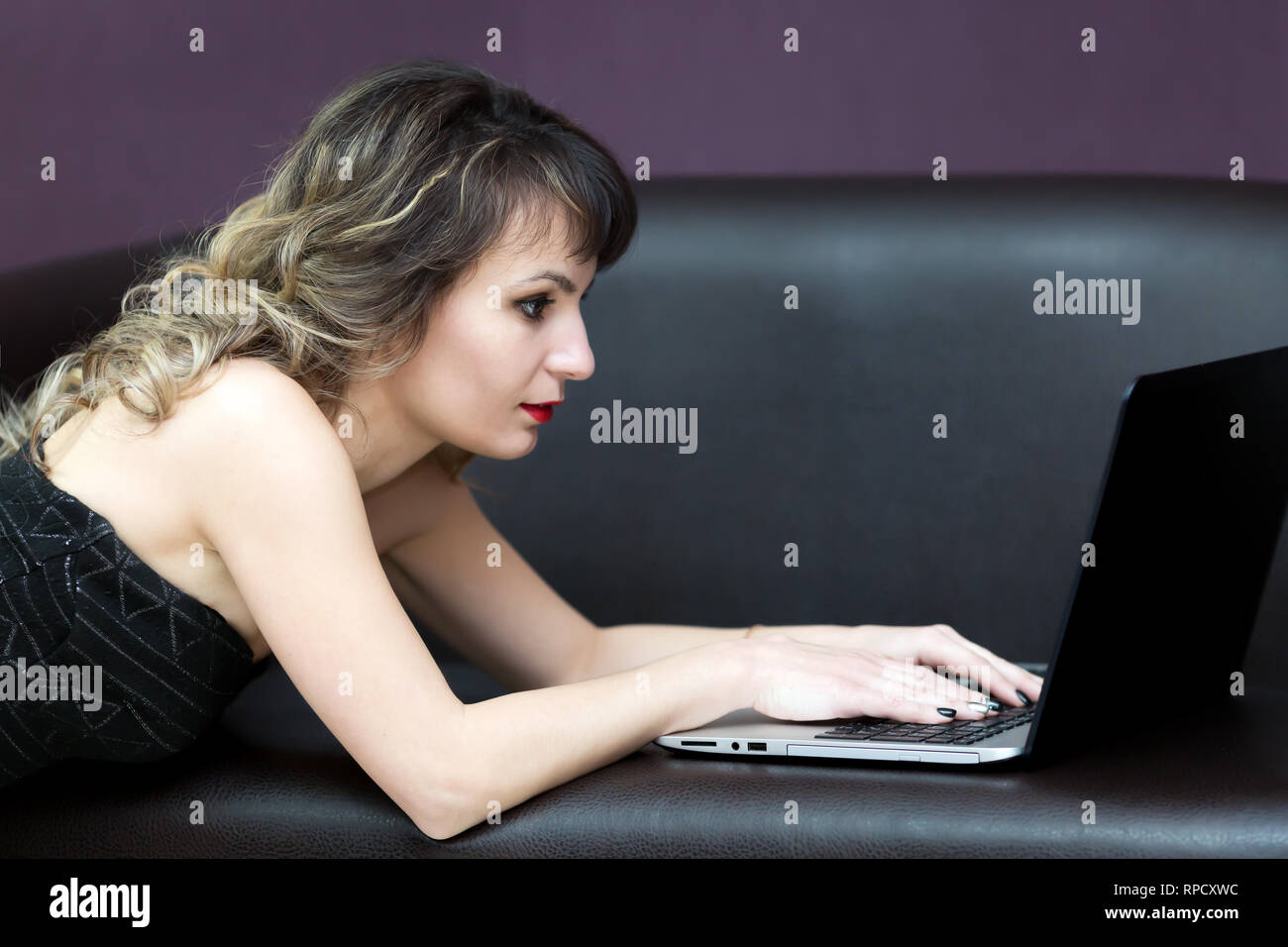 Une fille brune avec les cheveux ondulés travaille à un ordinateur. Banque D'Images