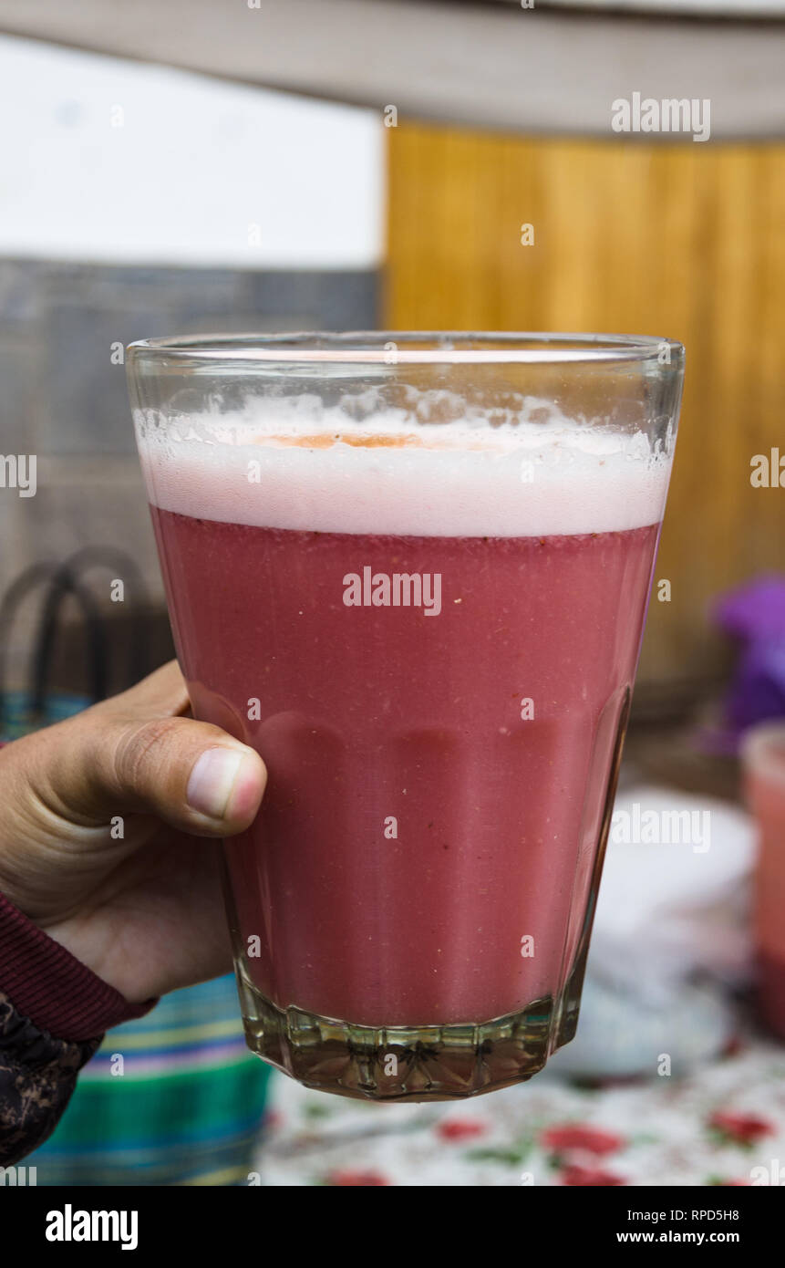 La main d'un homme tenant une tasse en verre avec jus de fraises acheté à la marché de Pisac à Cusco - Pérou Banque D'Images