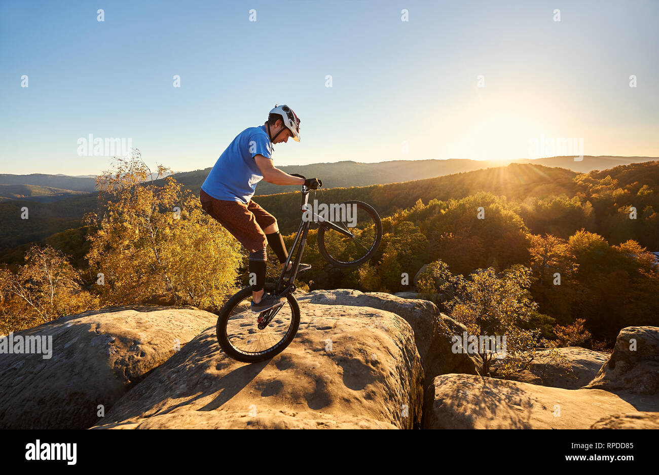 Cycliste professionnel équitation sur roue arrière à l'essai vélo. Sportsman rider en équilibre sur le bord du gros rocher sur le sommet de la montagne au coucher du soleil. Concept de sport extrême de vie actif Banque D'Images