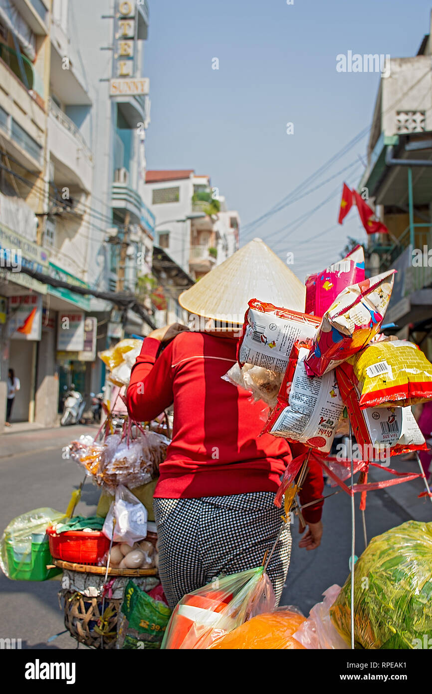 Un commerçant vietnamien femelle porte ses produits tout au long de la rue. Banque D'Images