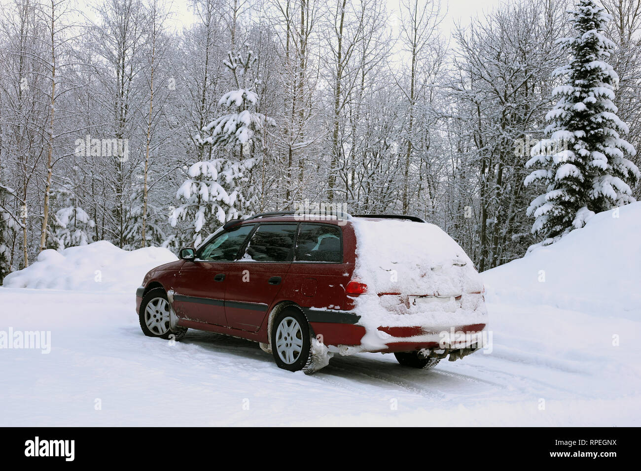L'hiver en Europe. Vieille voiture rouge dans un parking à côté d'une forêt couverte de neige. Il y a beaucoup de nature neige autour de la voiture. Photo de jour. Banque D'Images