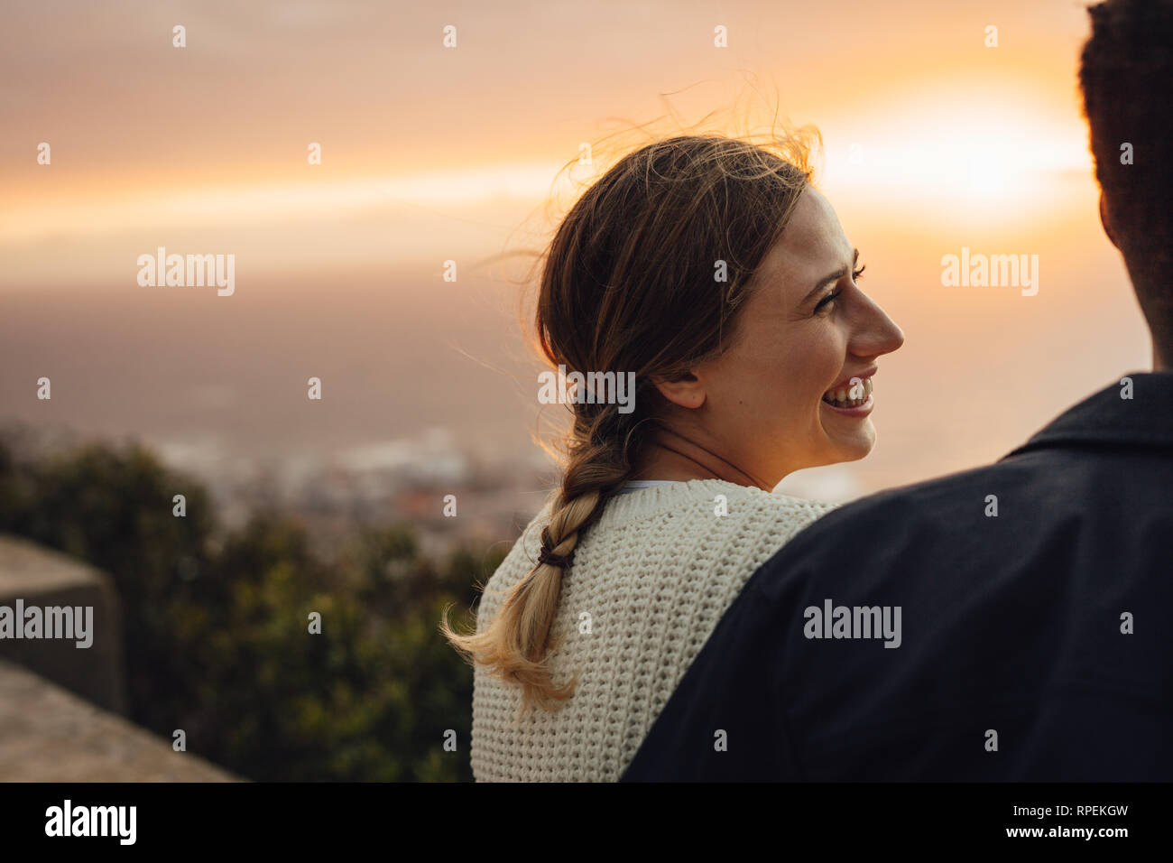 Cheerful young woman sitting avec son petit ami à l'extérieur. Femme à la recherche de son homme et souriant contre le coucher du soleil. Banque D'Images